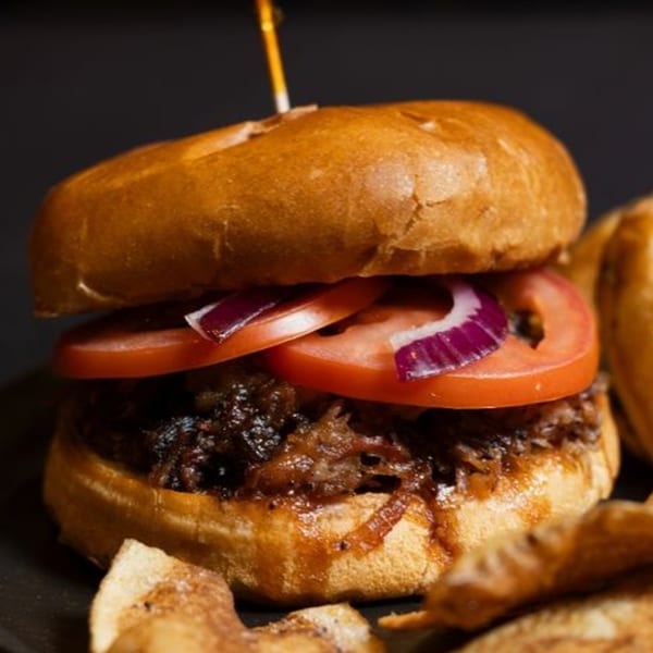Close-up of a pulled pork sandwich with tomatoes and red onions, served with potato chips.