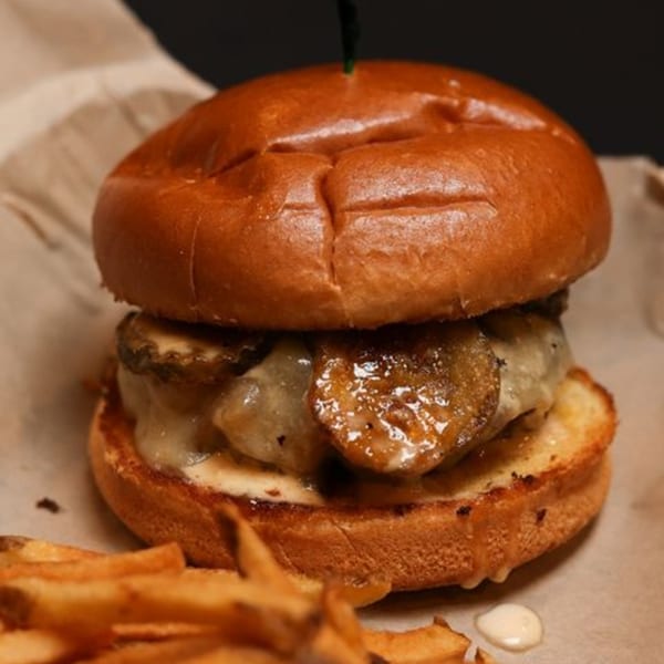 Close-up of a juicy burger with melted cheese and fried pickles, served with fries.