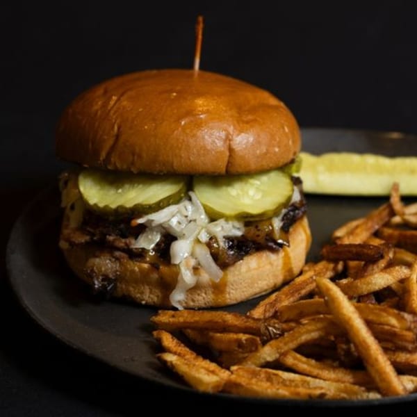 A pulled pork sandwich with pickles and coleslaw, served with fries and a pickle spear.