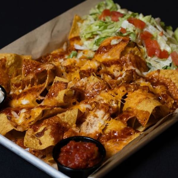 A tray of cheesy nachos with salsa, sour cream, shredded lettuce, and diced tomatoes.