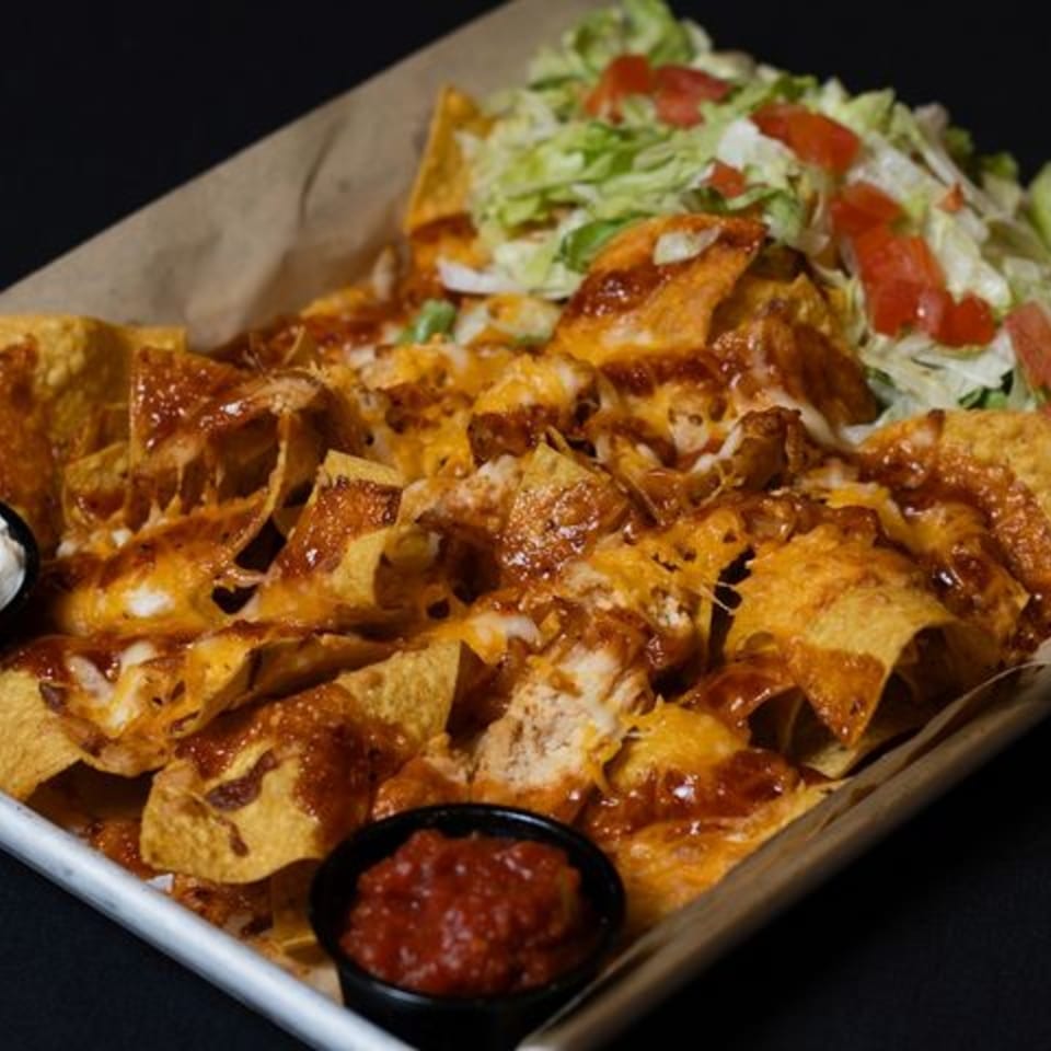 A tray of cheesy nachos with salsa, sour cream, shredded lettuce, and diced tomatoes.